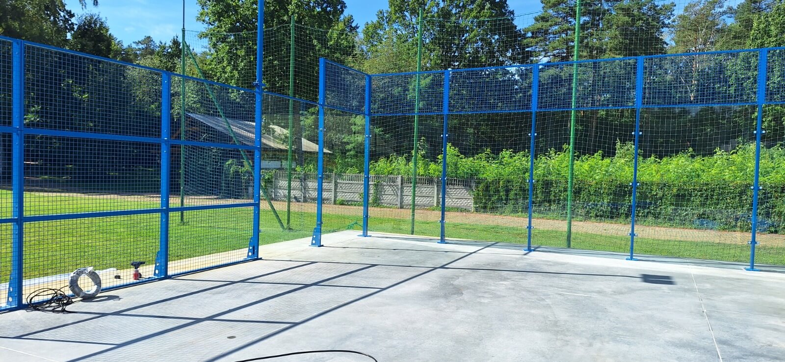 Kort do padla w budowie — niebieska konstrukcja stalowa z ogrodzeniem z siatki na betonowej płycie