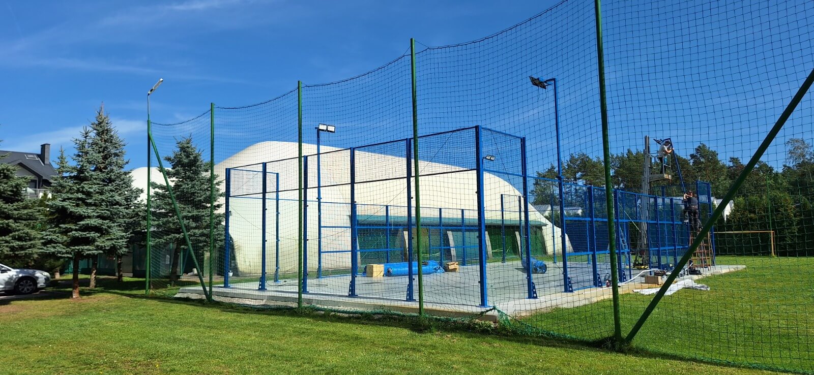 Gotowy kort do padla przy hali sportowej — widok od strony trawnika