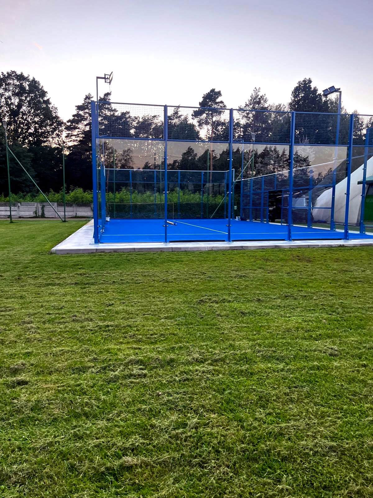 Gotowy kort do padla na betonowej płycie, widok od strony trawnika